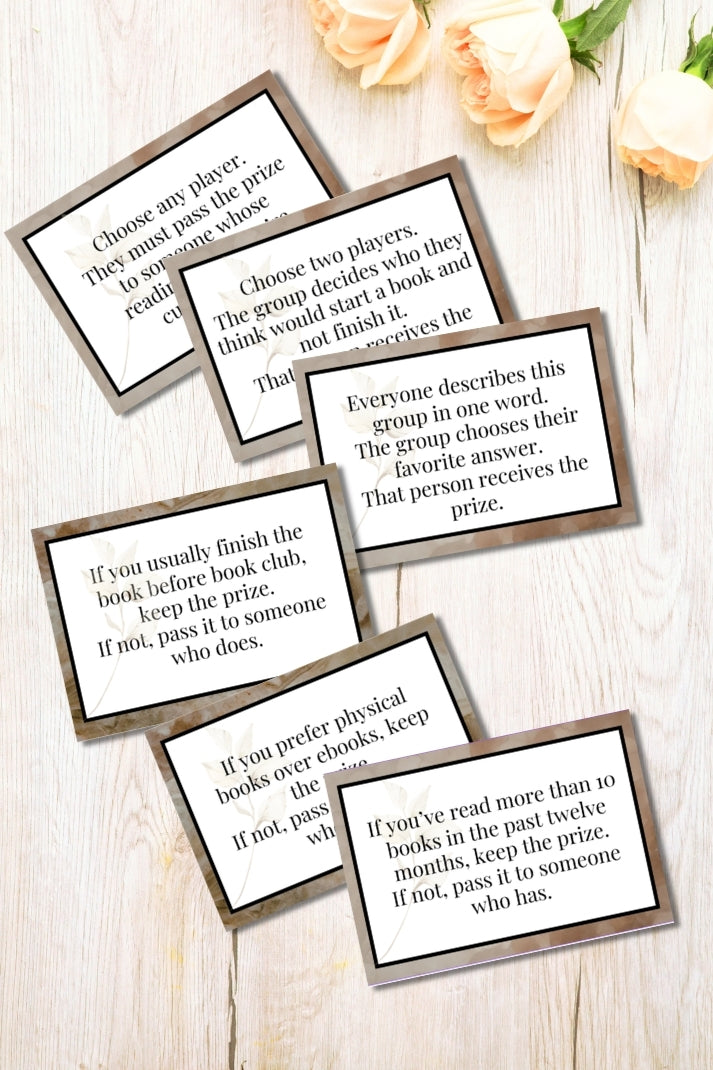 Set of book club game cards on a wooden surface with flowers in the background