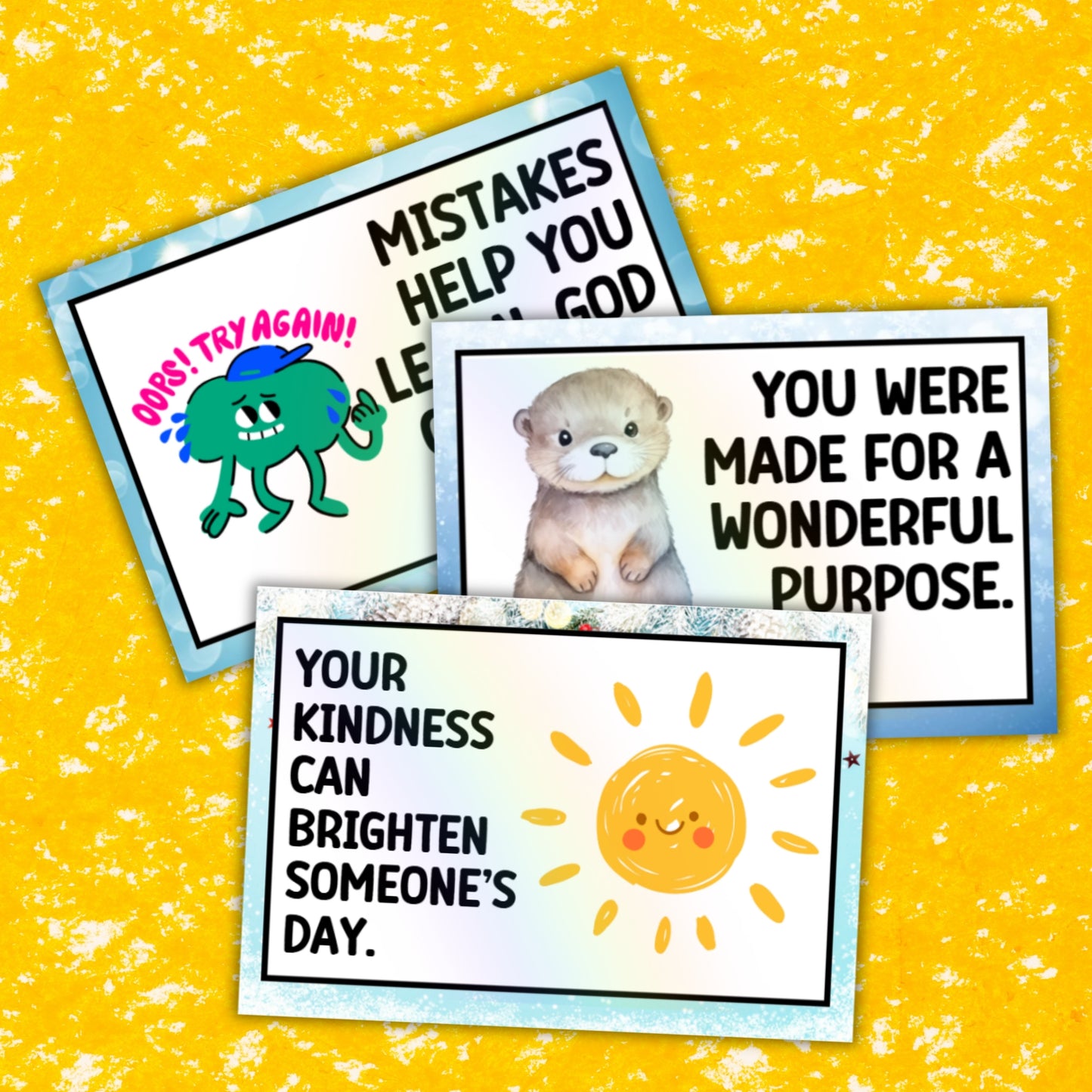 Three printed positivity cards arranged on a bright yellow textured background. The cards have white centers with black text and colorful illustrations: a green cartoon character with 'Oops! Try Again!', a otter with 'You Were Made for a Wonderful Purpose.
